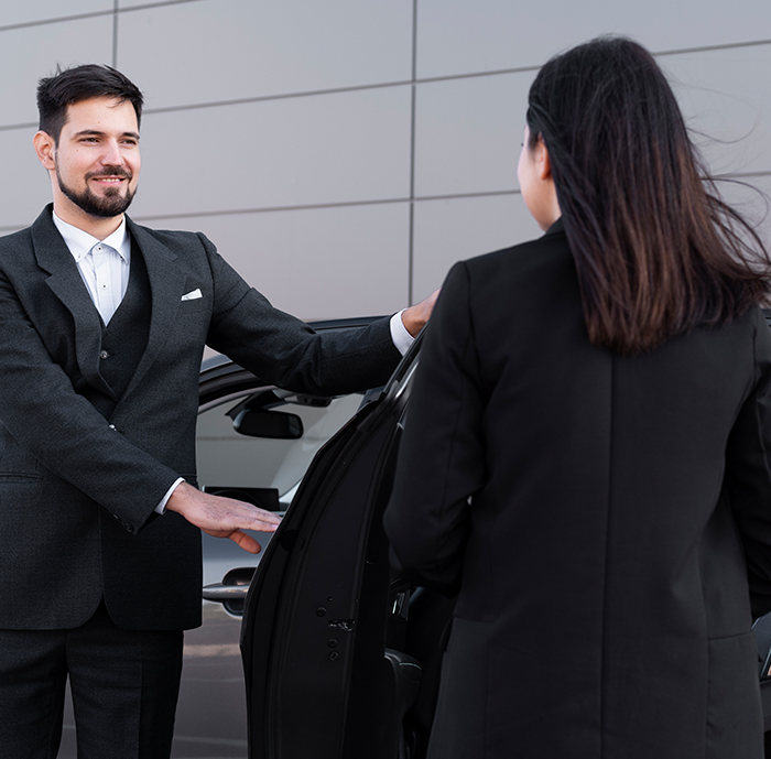 Professional chauffeur closing the door of a black luxury car for an executive passenger